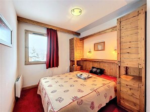 Een slaapkamer met een bed, een raam met gordijnen, een spiegel en een wandlamp.