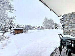 A snow-covered outdoor area with a stone building, a wooden structure, and a table with chairs. - Charming apartment with covered parking - 4 guests (La Toussuire)