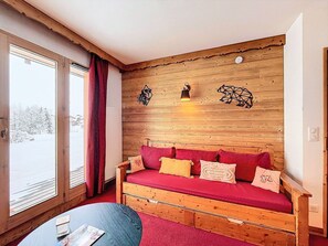 Een knus vertrek met een houten wand, een rode bank en een kleine tafel.