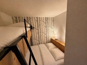 Habitación con literas, un mural en la pared, una mesita de noche con lámpara y un cabecero de madera.