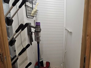 Ein schmales Badezimmer mit einem Händetrockner, einem Mopp und einem Besen, die an der Wand lehnen.