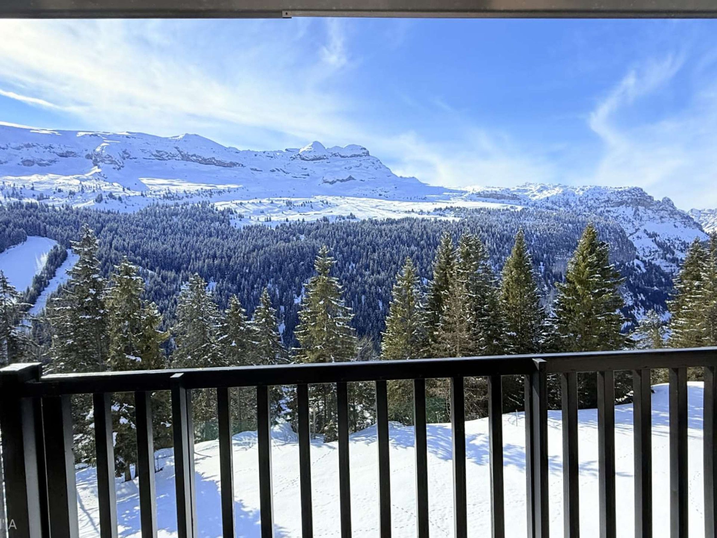A snow-covered mountain landscape with a forested valley and a clear sky.