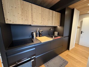 Eine moderne Küche mit schwarzen Schränken, einer Holz Arbeitsplatte, einem Einbauofen und einem Edelstahl-Spülbecken.
