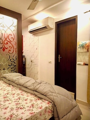 Un dormitorio con cama, unidad de aire acondicionado, una puerta y una pared con panel decorativo.