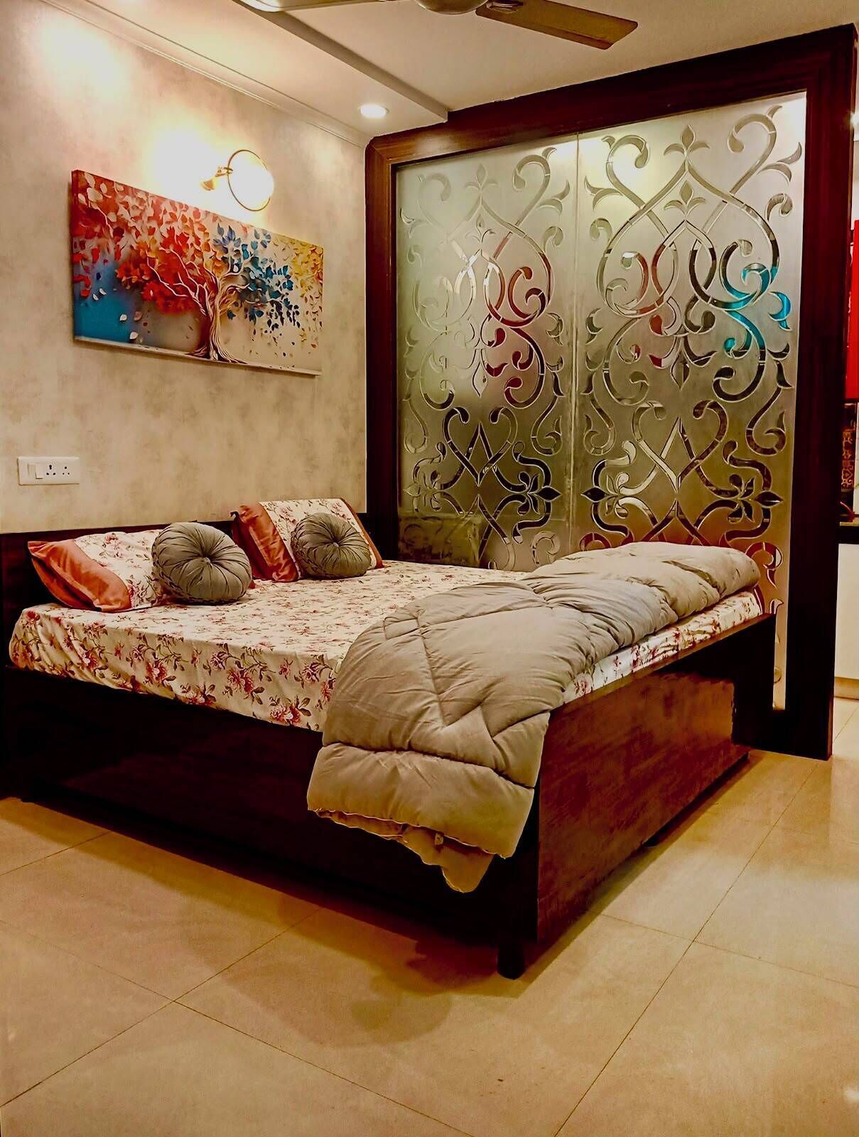 Un lit avec une couvre-lit à motifs floraux et plusieurs oreillers, un mur décoratif orné d’un tableau coloré et un ventilateur de plafond moderne.