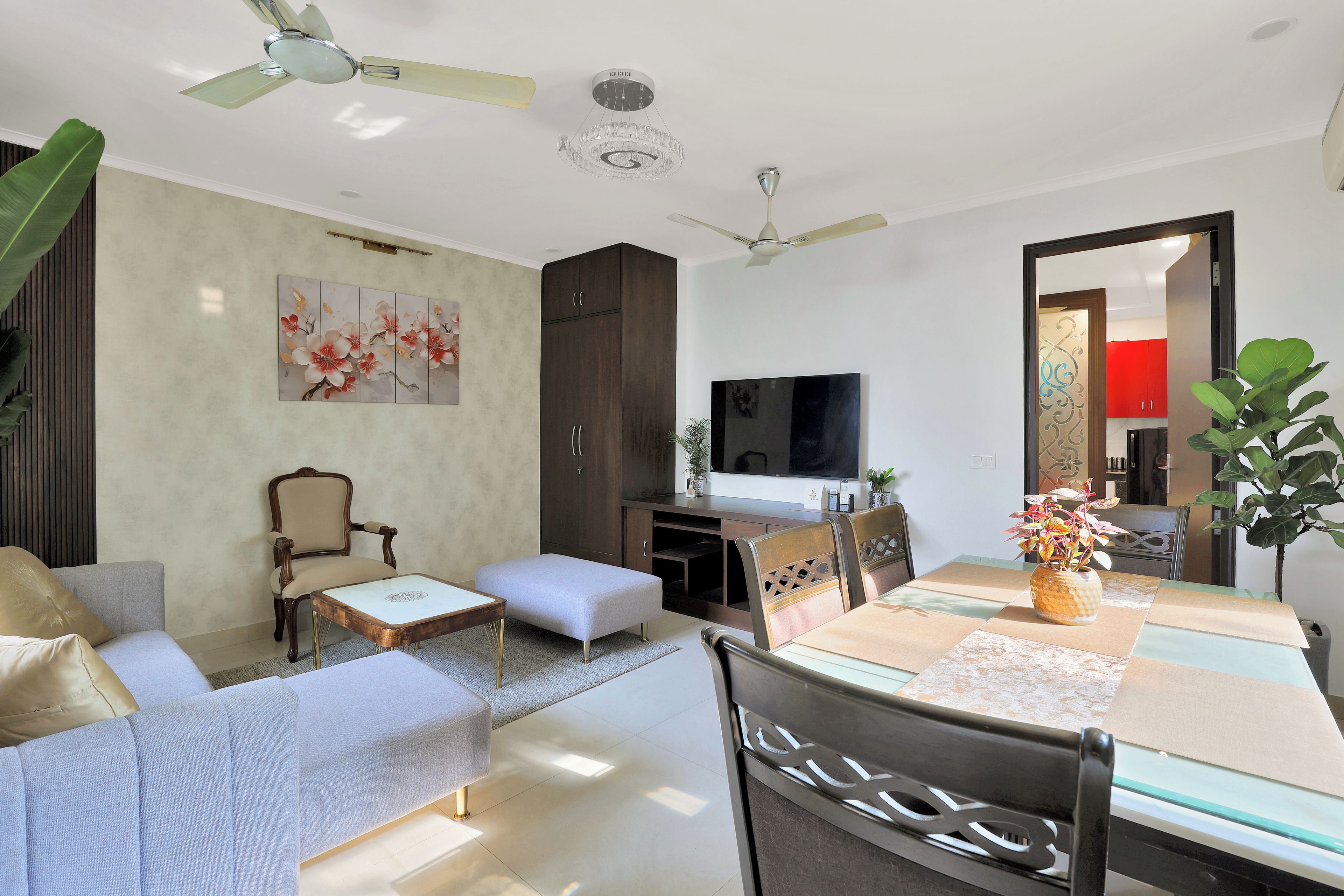 Un salon moderne comprenant un canapé, un pouf, une table à manger, des chaises, un téléviseur, des ventilateurs de plafond et un élément décoratif mural.