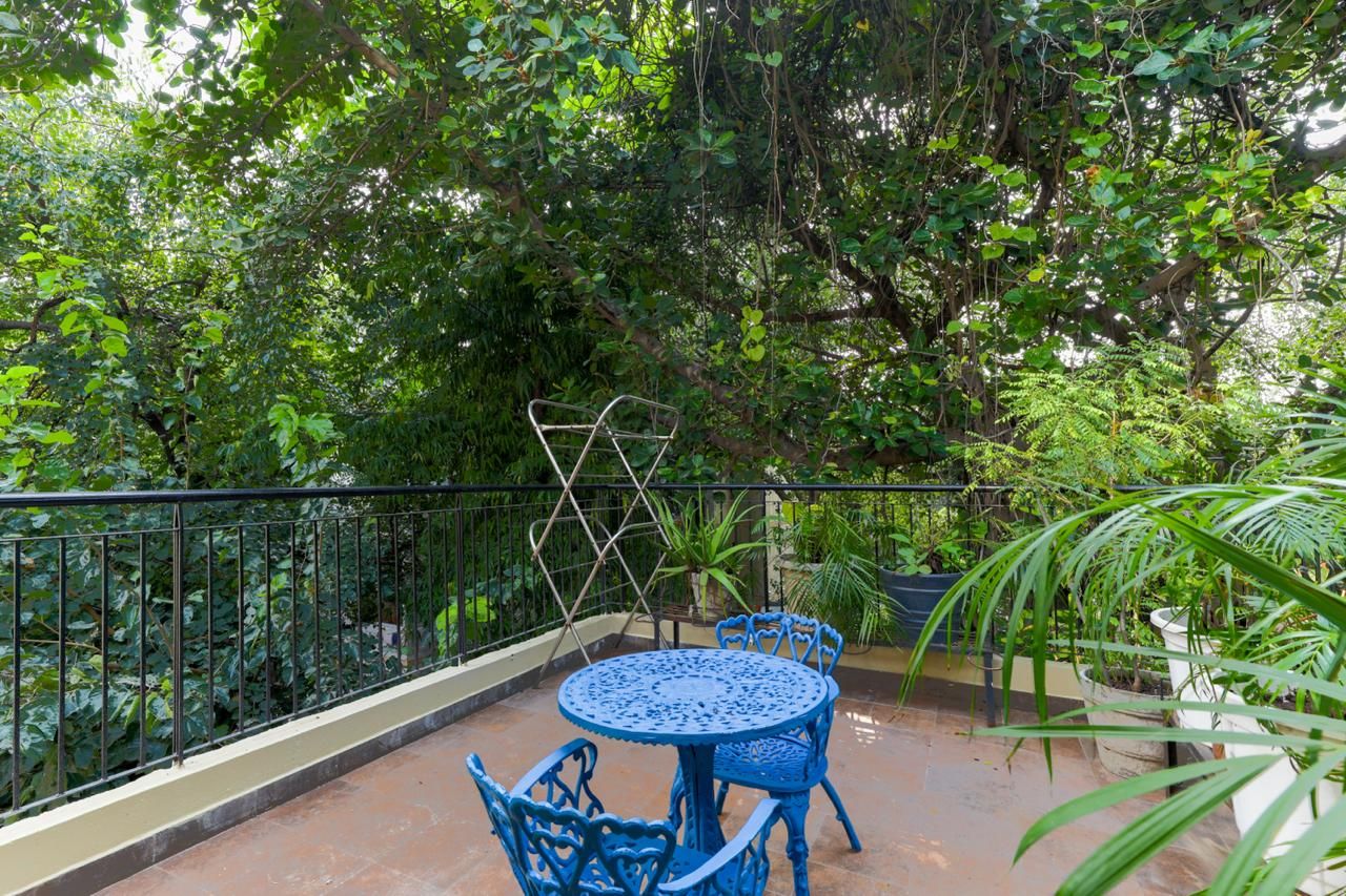 Ein Balkon mit blauem Metalltisch und -stühlen, umgeben von üppigem Grün und einem Metallgeländer.