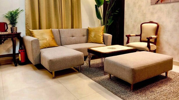 Un salon avec un canapé d’angle gris, une petite table basse, une chaise en bois et une grande plante.