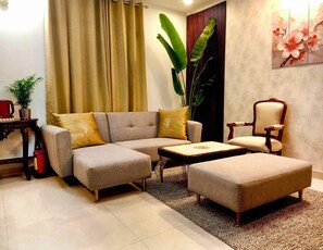 Una sala de estar con un sofá seccional gris, una mesita de centro pequeña, una silla de madera y una planta grande.