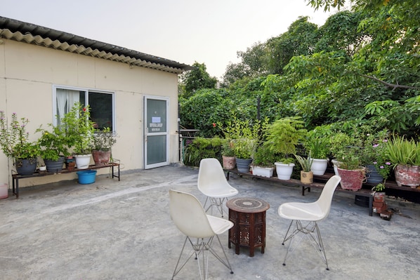 An outdoor patio with two white chairs, a small round table, and various potted plants.