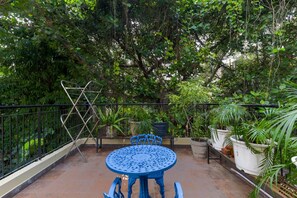 Una mesa y sillas de metal azul en un balcón con vistas a abundante vegetación y árboles.