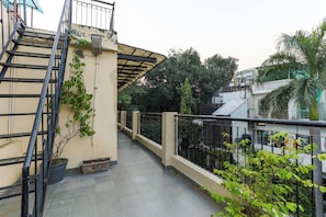 A narrow outdoor corridor with a tiled floor, metal railings, and a staircase on the left.