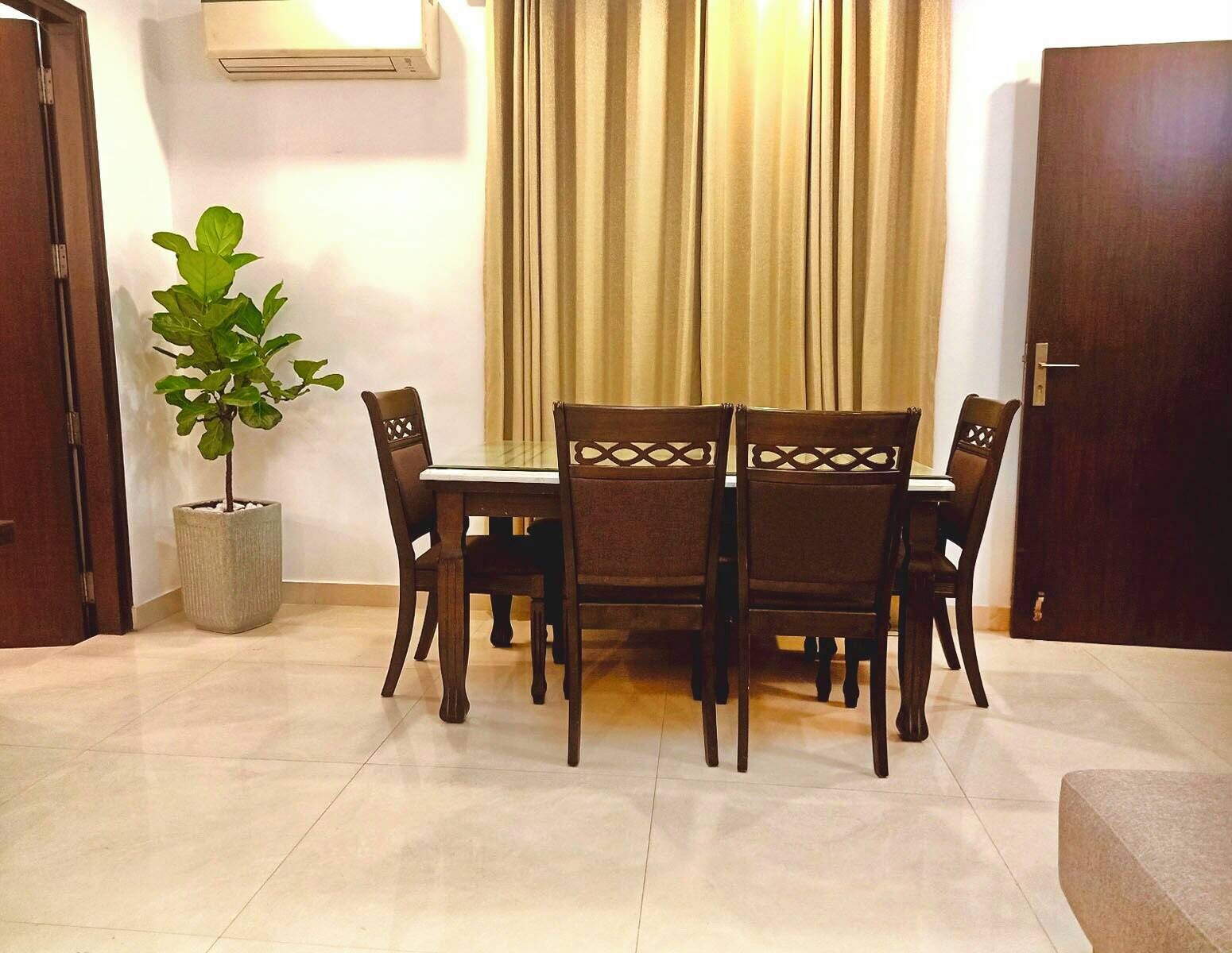 Un coin repas avec une table et des chaises, une plante en pot et une porte fermée.