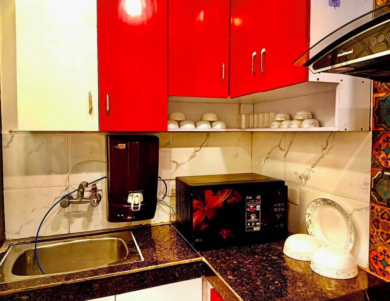 Une cuisine équipée d’un évier, d’un four à micro-ondes et de meubles de rangement rouges.