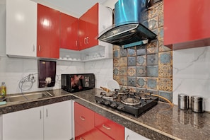 A kitchen with red cabinets, a gas stove, a microwave, and a water dispenser.