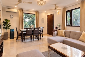 A modern living room with a sofa, dining table, chairs, a coffee table, a potted plant, and a ceiling fan.