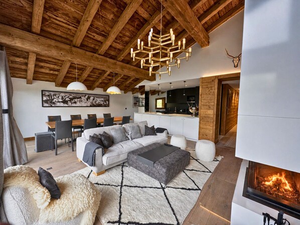 A modern living room with a fireplace, wooden ceiling beams, and a dining area with a large painting. - Comfortable apartment valley view - 10 guests (Saint-Martin-de-Belleville)