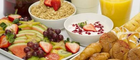 Una bandeja de desayuno con frutas, yogur, croissants y jugo.