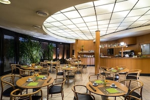A restaurant with round tables, chairs, and a bar area. - Hotel La Pioppa (Bologna)