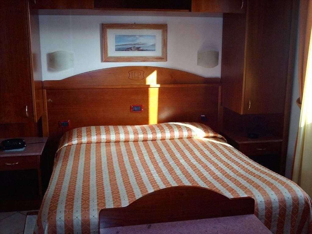 A hotel room with a bed, a nightstand, a lamp, a framed picture on the wall, and a wooden headboard.