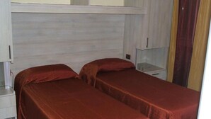 Une chambre avec deux lits, chacun recouvert d’une courtepointe rouge, et comprenant une table de chevet blanche et une petite table.
