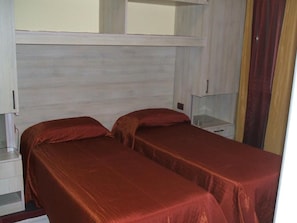 A room with two beds, each with a red bedspread, a white nightstand, and a small table. - Hotel La Pioppa (Bologna)