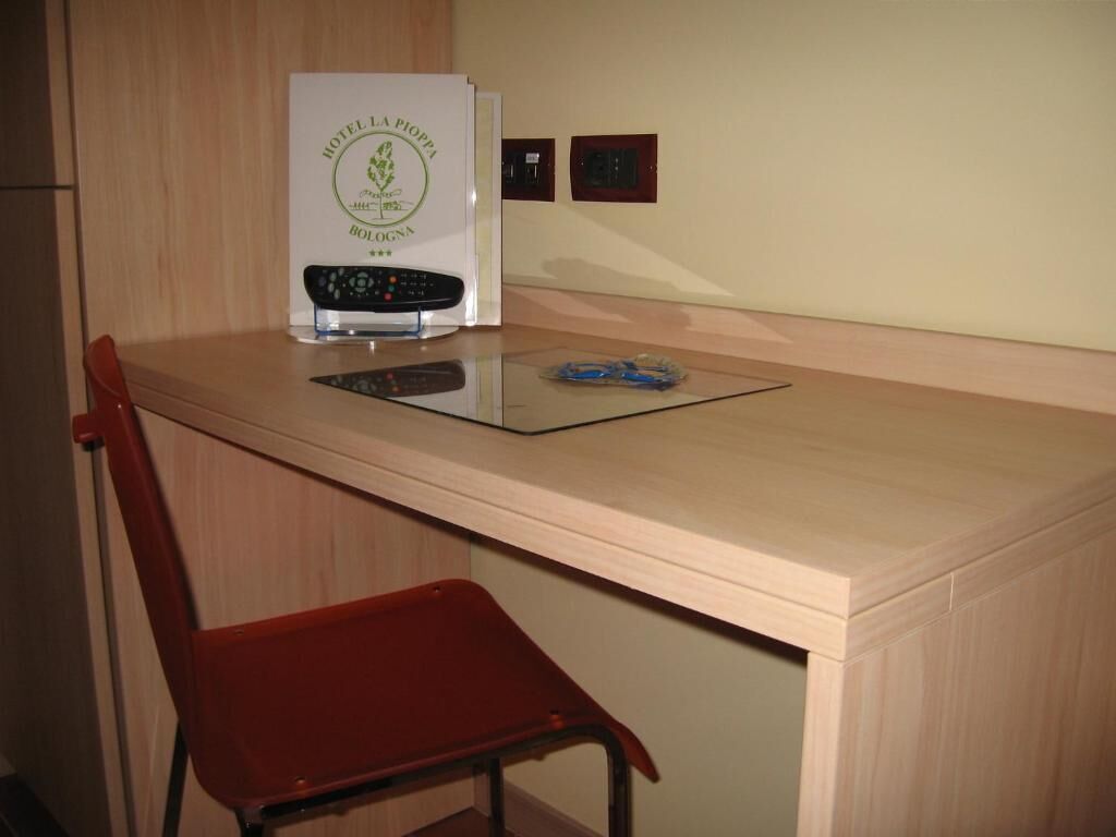 Habitación de hotel con un escritorio de madera, una silla roja, un control remoto y un certificado enmarcado en la pared.