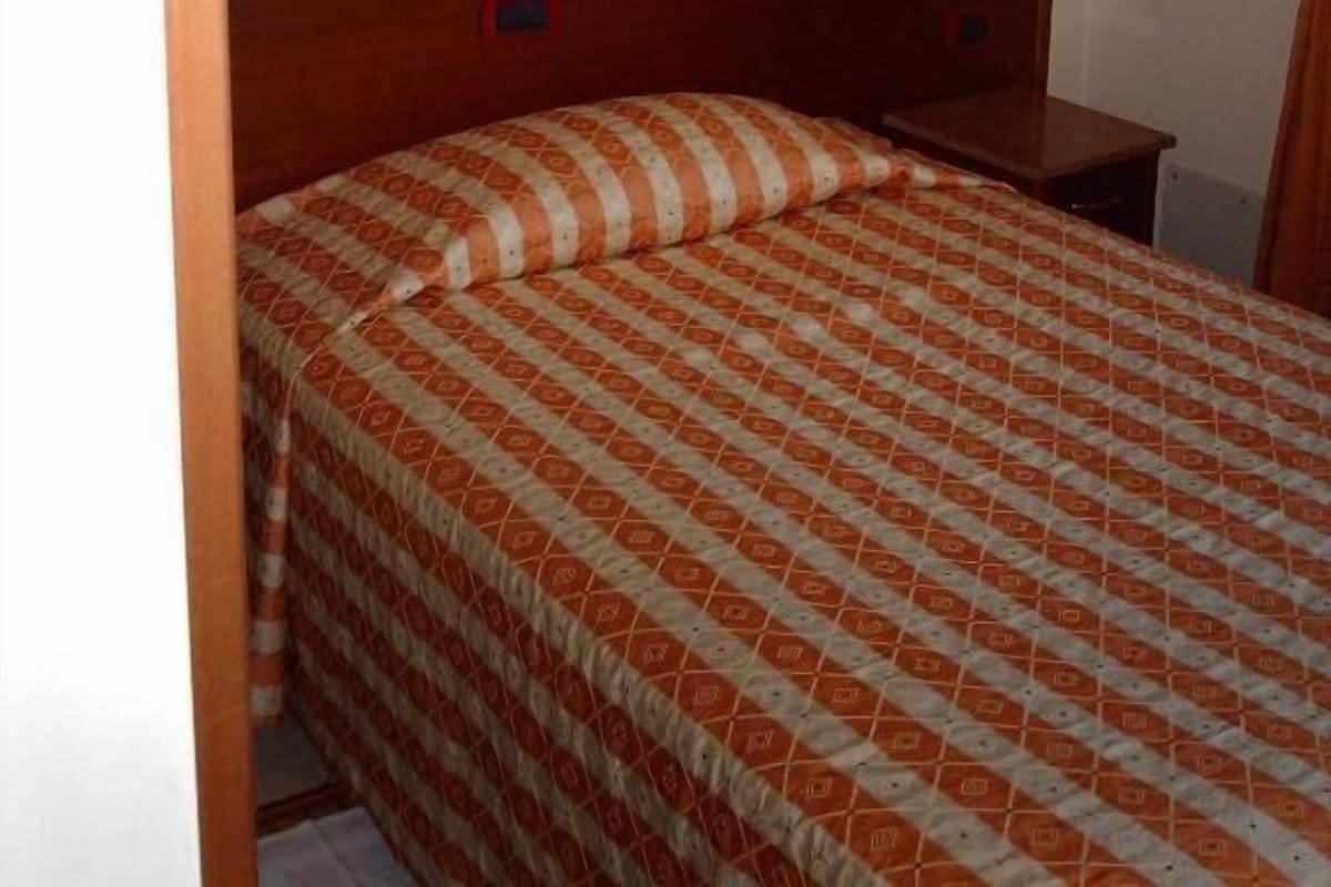 Une chambre à coucher avec une tête de lit en bois, un lit recouvert d’une couvre-lit à motifs orange et blanc, une table de chevet et un tableau encadré accroché au mur.