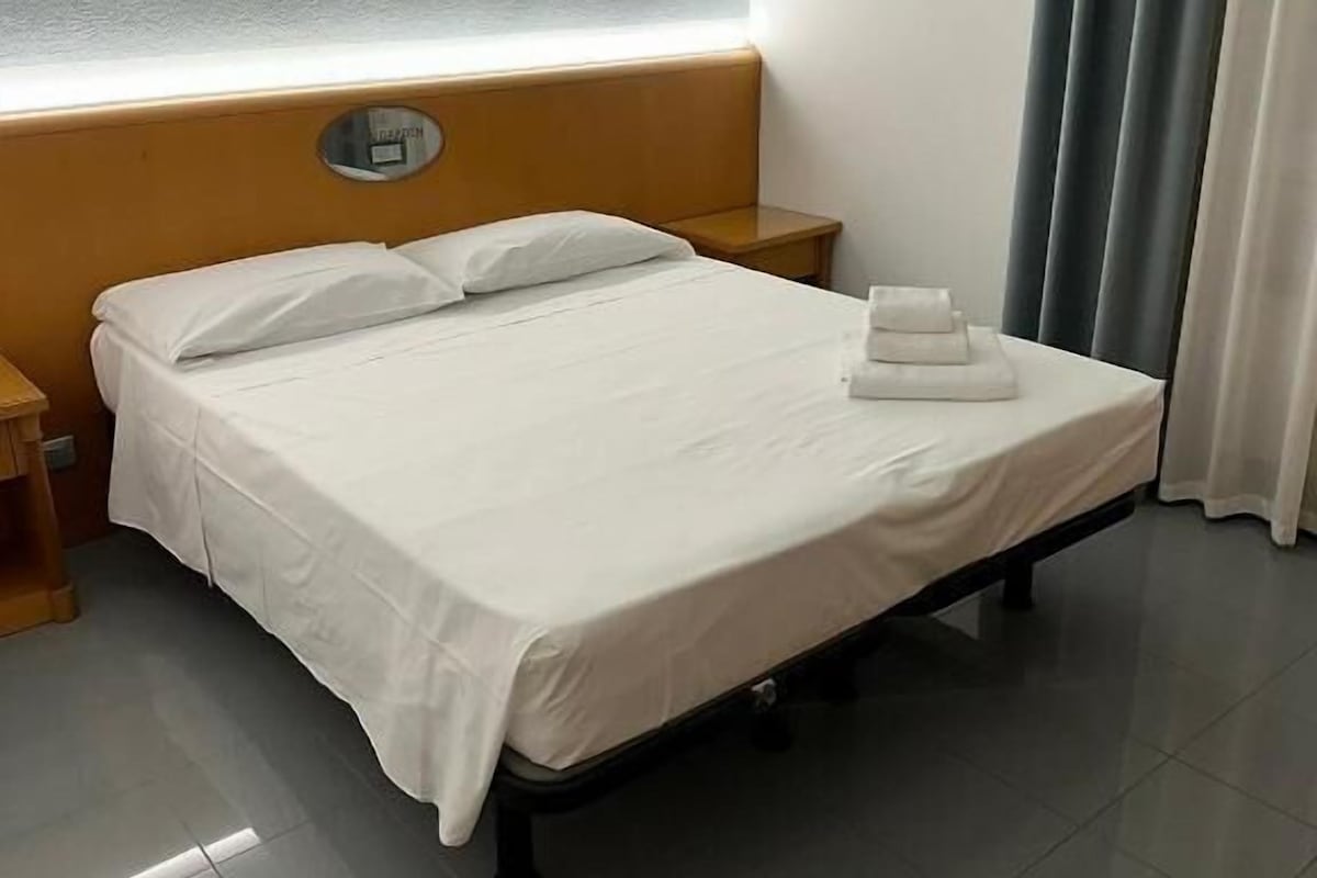 Une chambre d’hôtel avec un lit, une table de chevet, une horloge murale et un rideau.