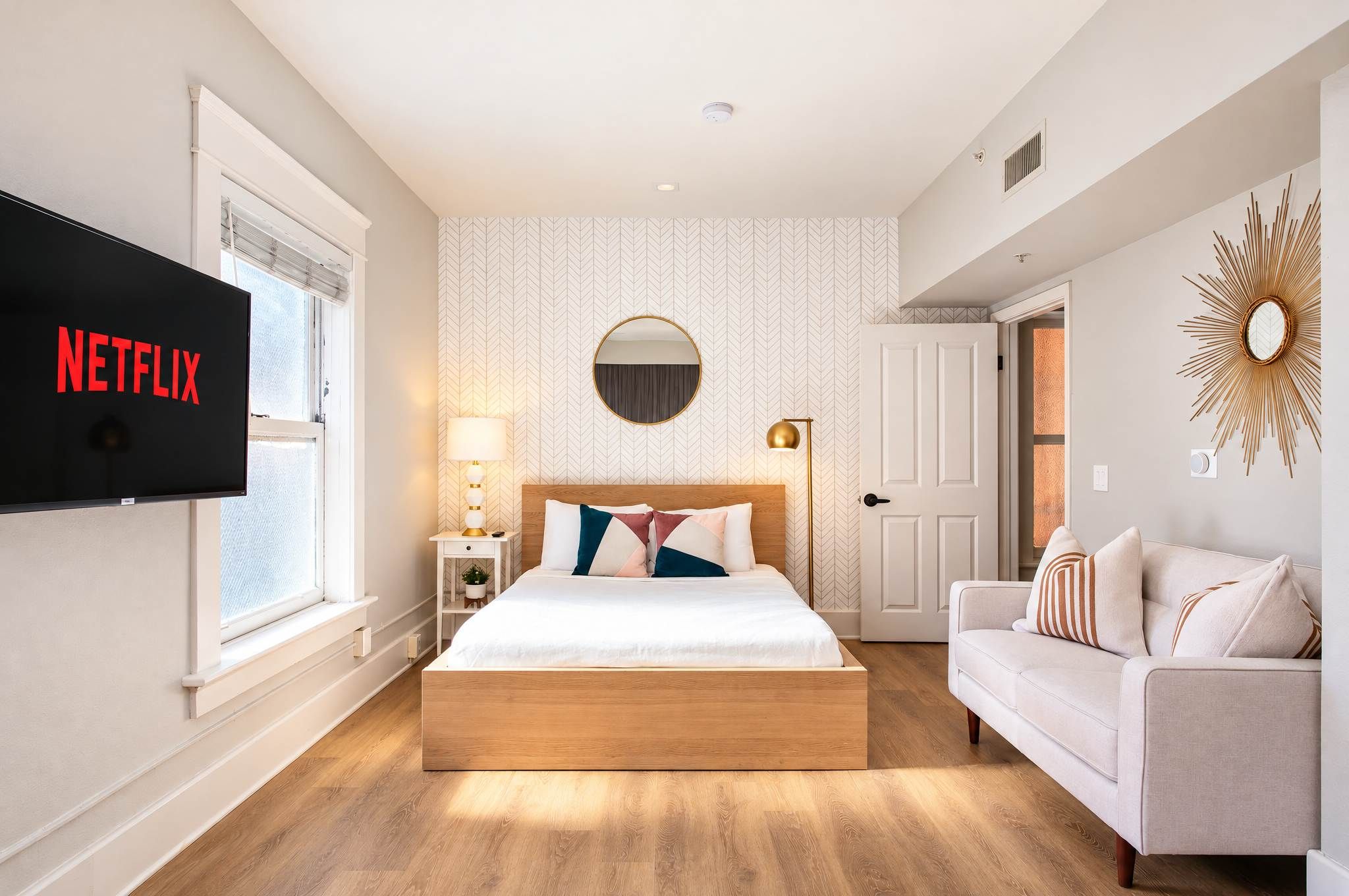 Een moderne slaapkamer met een bed, een televisie, een bank en een decoratieve spiegel.
