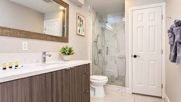 Un baño moderno con ducha de mármol, inodoro blanco y tocador de madera.