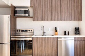 A modern kitchen with stainless steel appliances, a microwave, an oven, a dishwasher, and wooden cabinetry. - The Penn Hotel - Queen Bed, AC & Walk to Gaslamp!! (San Diego)