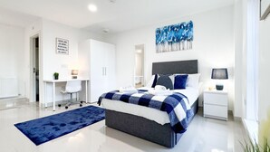 Une chambre moderne avec un lit, une table de chevet, un bureau et un tapis bleu.