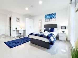 Un dormitorio moderno con cama, mesita de noche, escritorio y una alfombra azul.