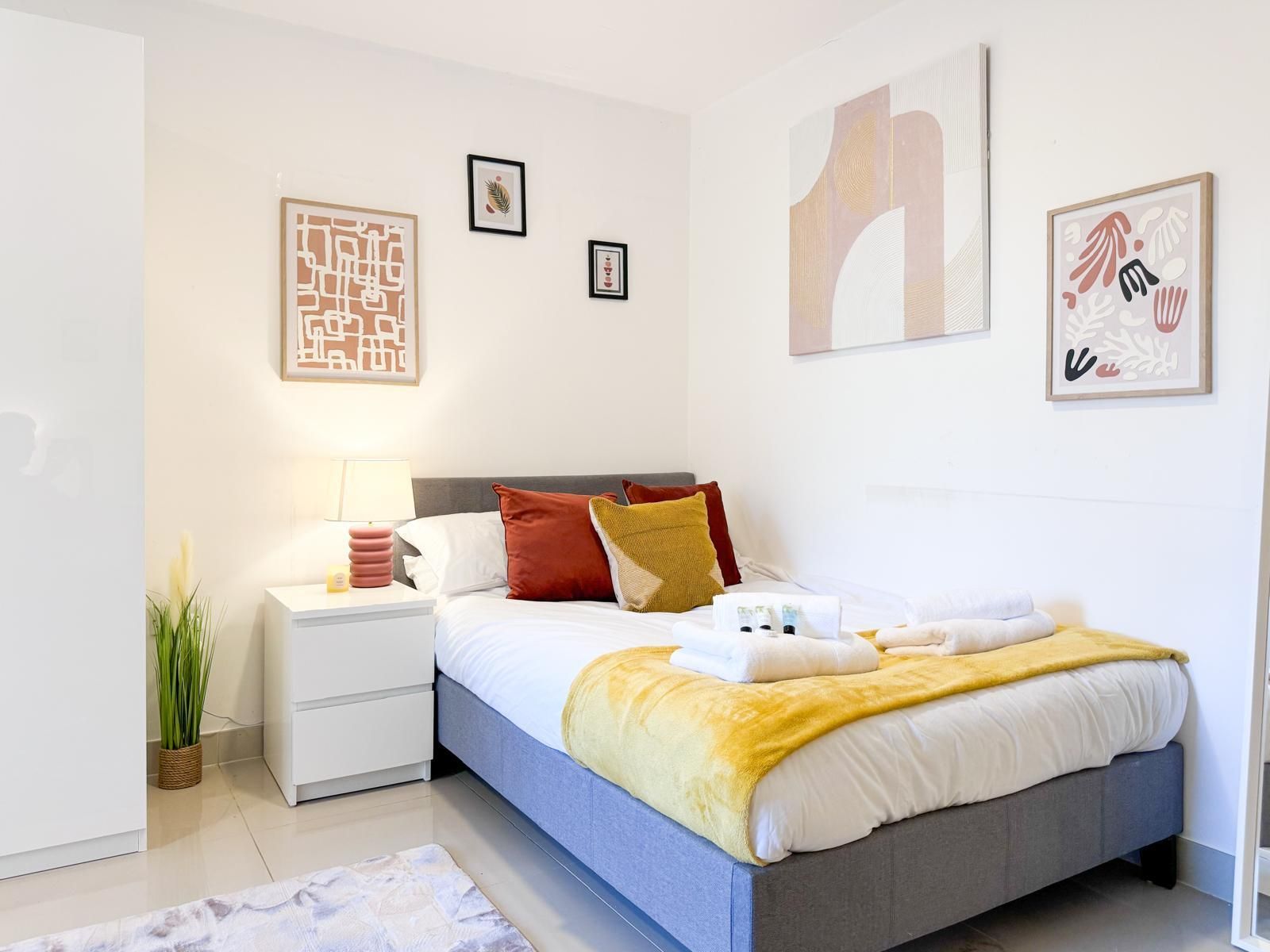 A modern bedroom with a bed, bedside tables, a nightstand, and wall art.