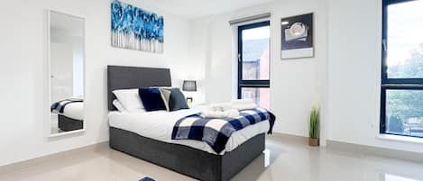 A modern bedroom with a large bed, a mirror, and a window.