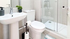 Une salle de bain moderne avec un lavabo blanc, des toilettes et une douche à parois de verre.