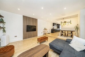 A modern living room with a flat-screen TV, wooden flooring, a sofa, and a dining area with a table and chairs. - Luxury 2 bed maisonette in Spitalfields zone 1 - Pass the Keys (London)