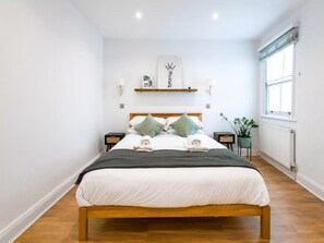 A modern bedroom with a wooden bed, white bedding, and a green plant by the window. - Luxury 2 bed maisonette in Spitalfields zone 1 - Pass the Keys (London)