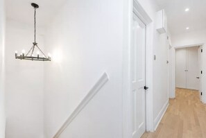 A hallway with white walls, a wooden floor, and a hanging light fixture. - Luxury 2 bed maisonette in Spitalfields zone 1 - Pass the Keys (London)