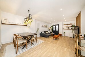 A spacious living area with a dining table, sofa, and a kitchen area with shelves. - Luxury 2 bed maisonette in Spitalfields zone 1 - Pass the Keys (London)