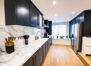 A modern kitchen with dark cabinets, a marble countertop, and a wooden floor. - Luxury 2 bed maisonette in Spitalfields zone 1 - Pass the Keys (London)