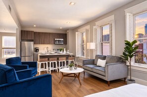 A modern living room with a grey sofa, blue armchairs, and a dining area with a white table. - The Penn Hotel - Designer 2BR Near Gaslamp & Park (San Diego)