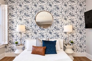 A bedroom with a bed, two bedside tables, a round mirror, and a patterned wallpaper. - The Penn Hotel - Designer 2BR Near Gaslamp & Park (San Diego)