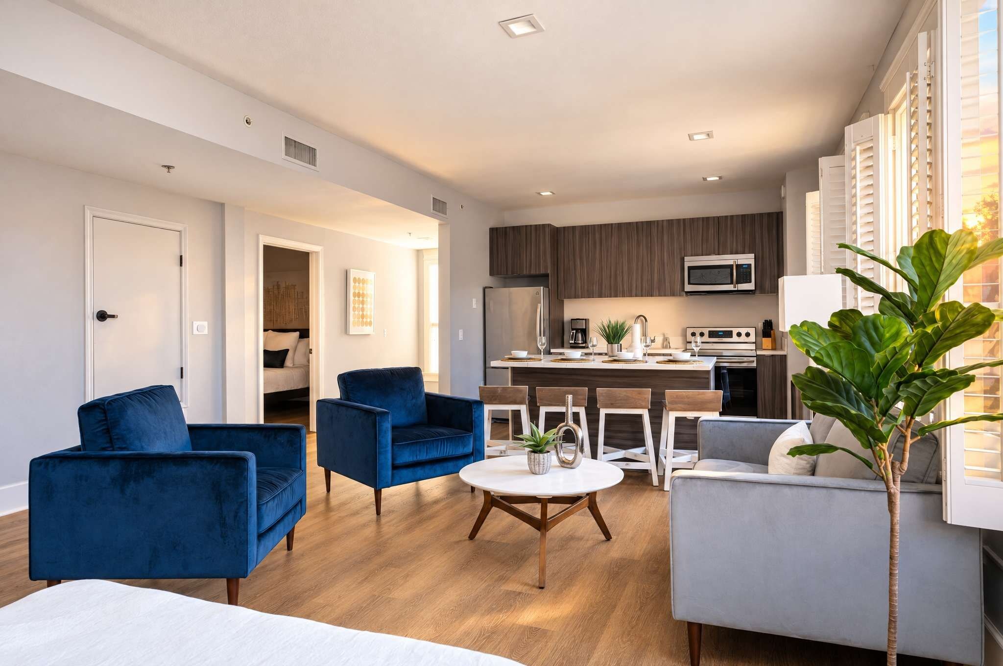 A modern living room with a sofa, chairs, a dining table, and a kitchen area with appliances.