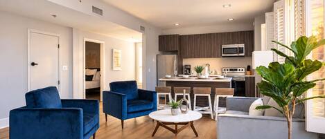 A modern living room with a sofa, chairs, a dining table, and a kitchen area with appliances.