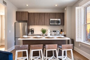 A modern kitchen with a central island, stainless steel appliances, and wooden cabinetry. - The Penn Hotel - Designer 2BR Near Gaslamp & Park (San Diego)