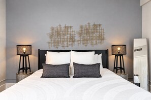 Un dormitorio con una cama, dos mesitas de noche con lámparas, una obra de arte en la pared y una puerta.