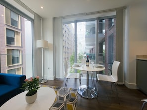 A modern living room with a round table, two white chairs, a blue sofa, and a potted plant. - Sleek flat near the City 5 min from station - Pass the Keys (London)