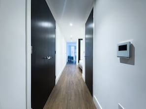 A hallway with dark wooden doors and a light-colored floor, leading to a room with a bed and a window. - Sleek flat near the City 5 min from station - Pass the Keys (London)
